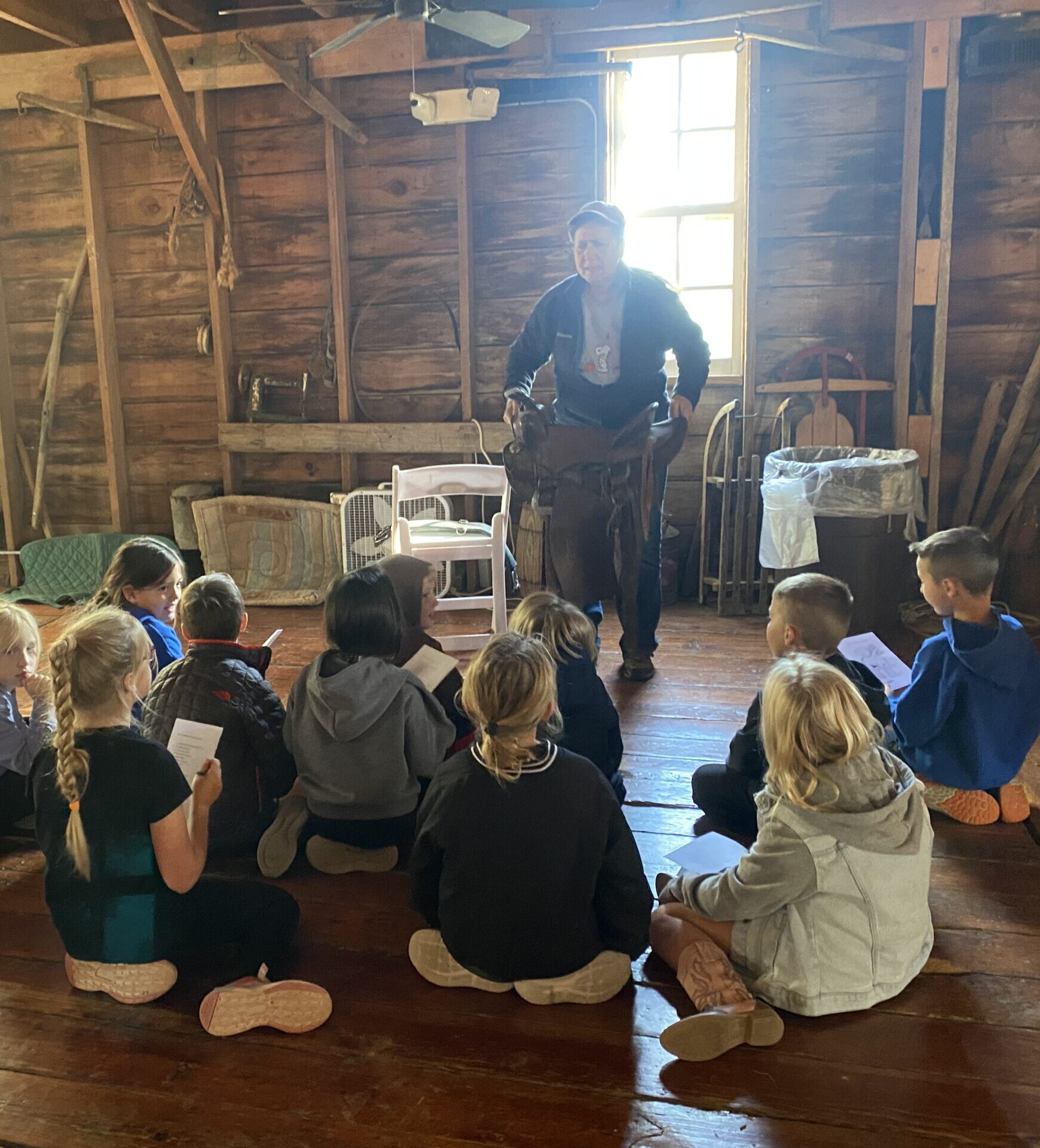 Workshop at S2S Ranch Instructor teaching kids about horses while holding a saddle.