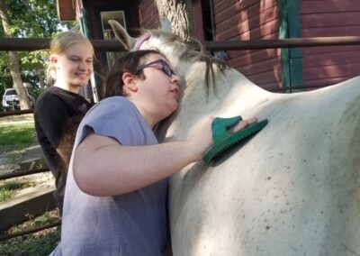 A girl who is leaning on a horse to groom it with assistance.